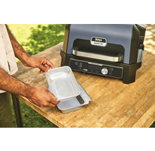 Gril électrique Ninja Woodfire avec une personne tenant un plat en aluminium