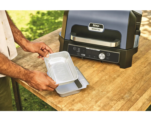 Gril électrique Ninja Woodfire avec une personne tenant un plat en aluminium