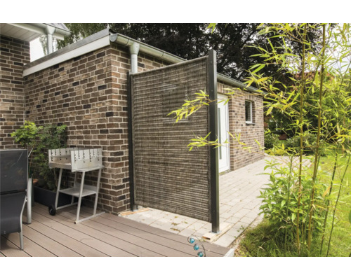 Außenbereich mit Sichtschutzwand, Grill und Gartenmöbeln auf einer Terrasse vor einem Backsteingebäude.