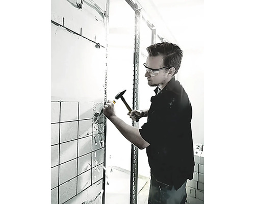 Un homme utilise un marteau et un burin pour retirer des carreaux d''un mur.