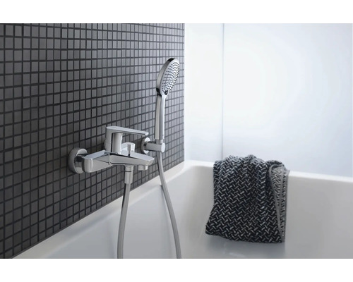 Badezimmerarmatur mit Handbrause an einer Mosaikwand über einer Badewanne.
