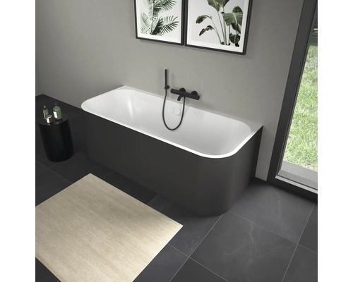 Baignoire îlot avec robinetterie noire dans une salle de bain avec œuvres d''art et tapis.