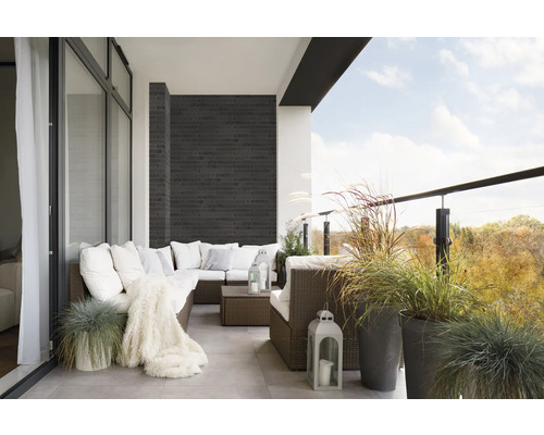 Balkon mit Rattansofa, Kissen, Decke, Laternen und Ziergräsern in Töpfen.