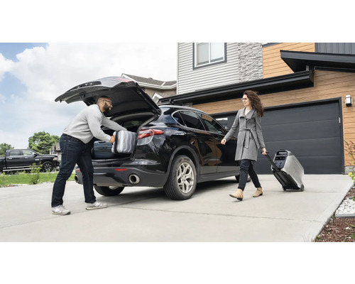 Un homme met des valises dans le coffre d''une voiture, tandis qu''une femme tire un générateur électrique portable sur roues.
