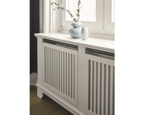 Cache-radiateur en bois avec des lamelles verticales et des objets de décoration sur le dessus.