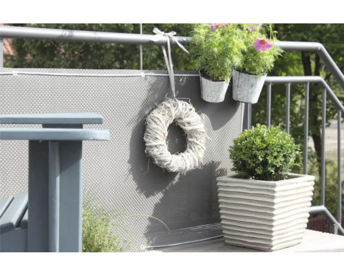 Dekorierter Balkon mit Sichtschutz, Tisch, Pflanzen und Kranz.