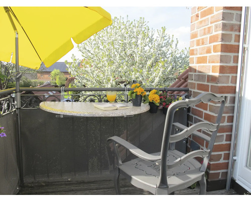 Balkonszene mit Sonnenschirm, Tisch, Stuhl, Getränk und Buch.