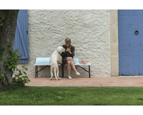 Frau mit Hund auf Gartenbank vor Hauswand