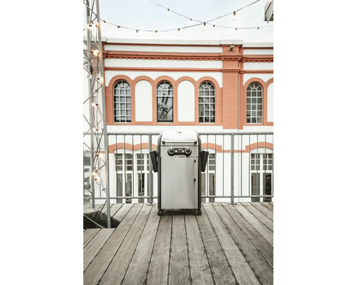 Barbecue à gaz en acier inoxydable sur une terrasse devant un immeuble