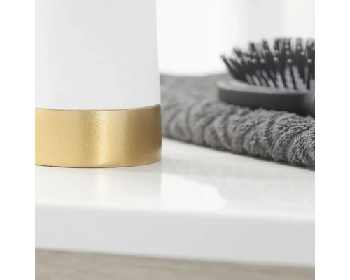 Detailansicht eines weißen Behälters mit goldfarbenem Akzent, eines grauen Handtuchs und einer Haarbürste