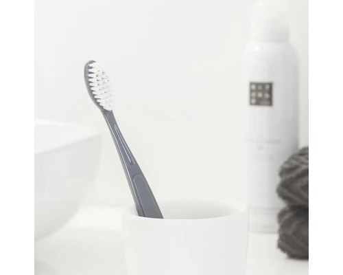 Graue Zahnbürste in einem weißen Becher