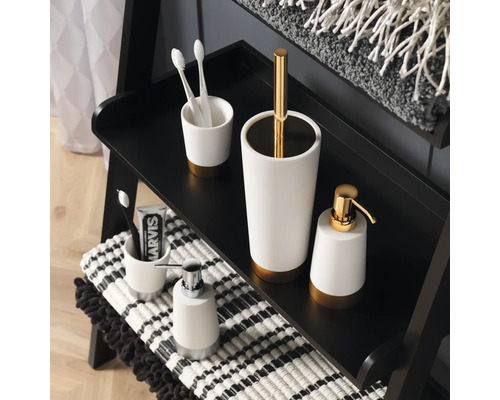 Badezimmer-Accessoires auf einem Regal: Seifenspender, Zahnputzbecher und WC-Garnitur.