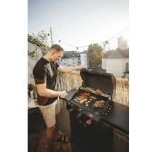 Un homme fait griller des légumes et de la viande sur un barbecue à gaz sur un balcon