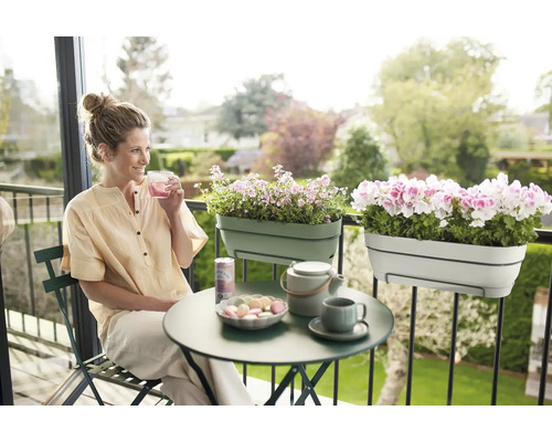 Frau sitzt auf Balkon mit Balkonkästen, Tisch und Getränken