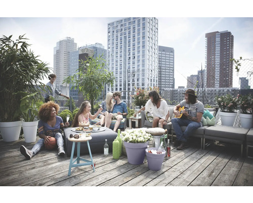 Groupe de personnes se détendant sur un toit-terrasse avec des meubles de jardin et des plantes en pot, avec un paysage urbain en arrière-plan