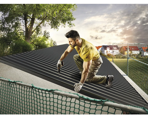 Un homme installe un toit en tôle trapézoïdale avec une visseuse sans fil.