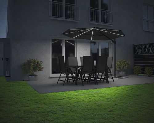 Beleuchteter Gartensitzplatz mit Sonnenschirm, Tisch und Stühlen in der Abenddämmerung.