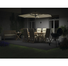 Gartenambiente mit beleuchtetem Sonnenschirm, Gartentisch, Stühlen, Grill und Bepflanzung bei Nacht.