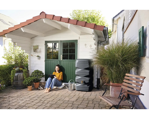 Scène de jardin avec une femme assise à côté d''un réservoir d''eau de pluie devant une cabane de jardin