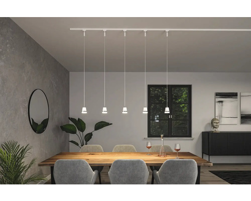 Esszimmer mit Esstisch, Stühlen, Zimmerpflanzen, Spiegel, Sideboard, Dekoration und einer weißen Schienenleuchte mit fünf Pendelleuchten.