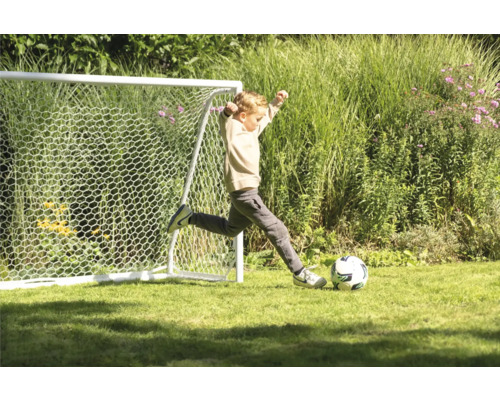 Un garçon tape dans un ballon de football devant un but de football dans le jardin