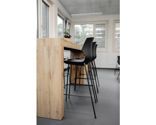 Scène avec table haute et tabourets de bar noirs dans une pièce lumineuse.