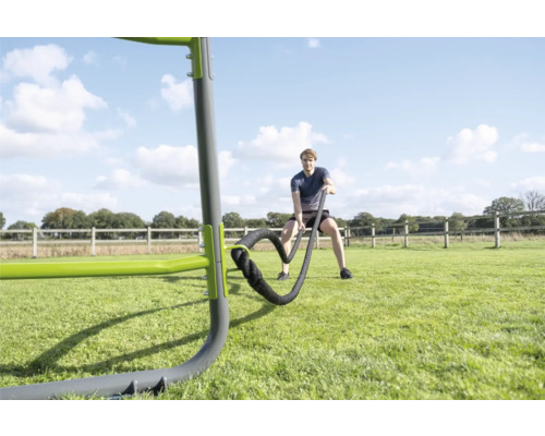 Mann trainiert mit Battle Rope an einer Outdoor-Fitnessanlage auf einer Wiese.