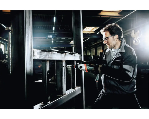 Un homme portant des lunettes de protection perce du métal avec une perceuse Metabo.