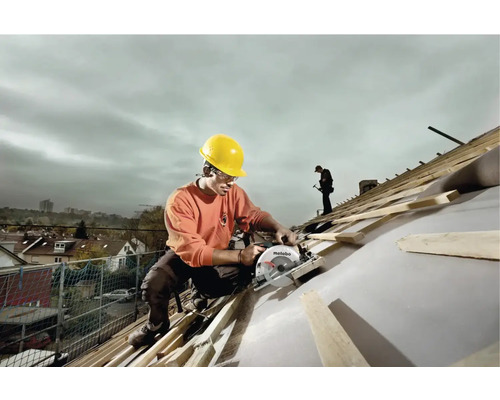 Un homme portant un casque de protection travaille avec une scie circulaire sur un toit.