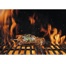 Un steak est grillé sur un barbecue avec des flammes.