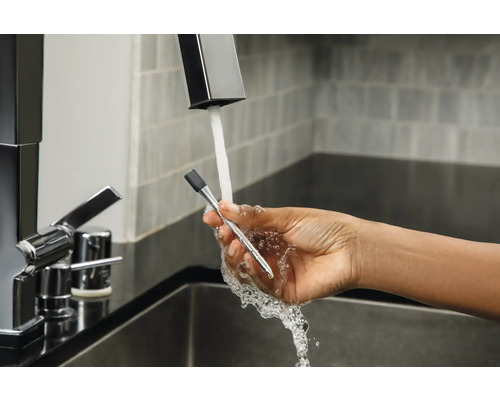 Eine Hand hält ein Thermometer unter einen Wasserhahn.