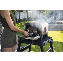 Une femme sort un rôti d''un barbecue d''extérieur.