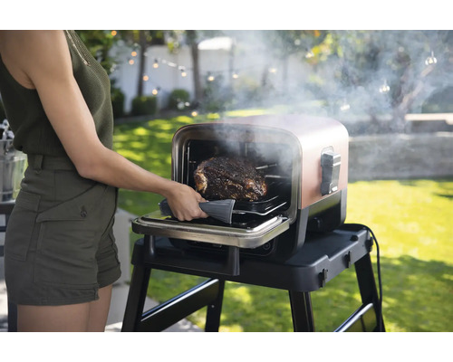 Eine Frau nimmt einen Braten aus einem Grill im Freien.
