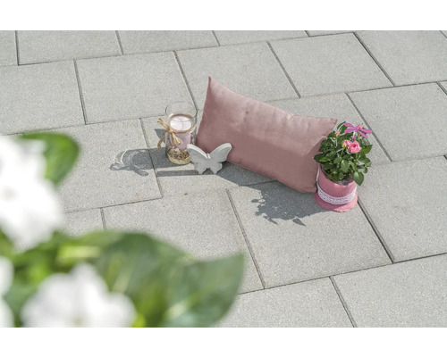 Scène de jardin décorative avec pavés, coussin, bougie, papillon et plante en pot