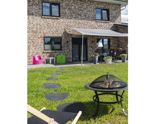 Aussenbereich mit Feuerstelle, Liegestuhl, Wegplatten und Beschattung vor einem Wohnhaus