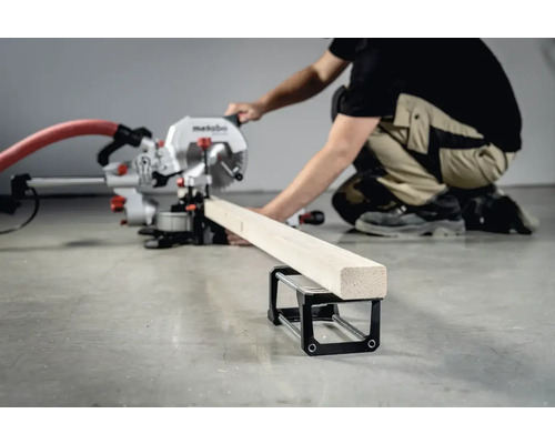 Eine Metabo Kappsäge beim Zuschneiden eines Holzstücks mit einer Werkstückauflage.