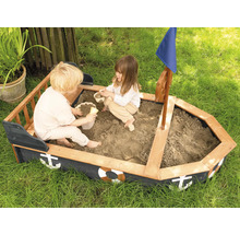 Zwei Kinder spielen in einem Sandkasten in Bootsform mit Steuerrad und Segel im Garten.