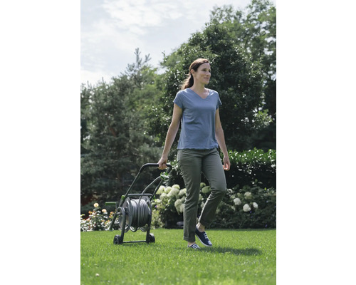 Frau schiebt einen Gartenschlauchwagen im Garten.