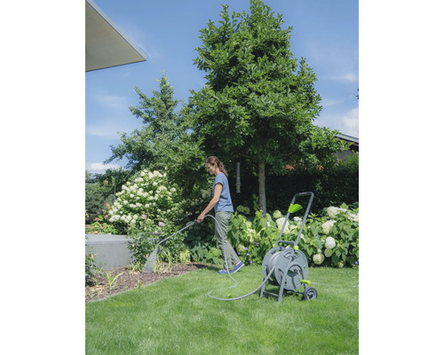 Frau giesst Pflanzen mit einem Gartenschlauch und einer Schlauchtrommel im Garten