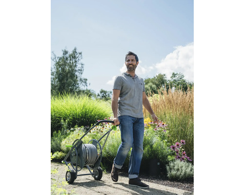 Ein Mann zieht einen Gartenschlauchwagen durch einen Garten.