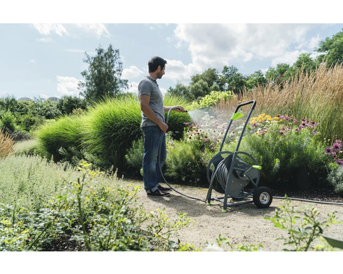 Ein Mann bewässert einen Garten mit einem Schlauchwagen.