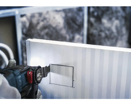 Une main découpe un rectangle dans un panneau isolant avec un outil multifonction.