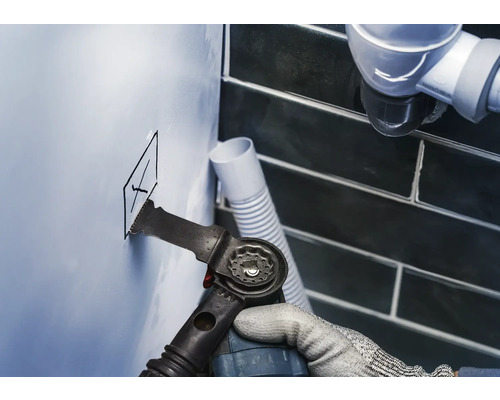 Outil multifonction oscillant coupant un trou dans un mur de salle de bain.