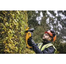 Un homme portant un casque et des lunettes de protection taille une haie avec un taille-haie sans fil DeWalt.