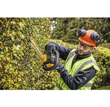 Une personne taille une haie avec un taille-haie tout en portant des vêtements de protection.