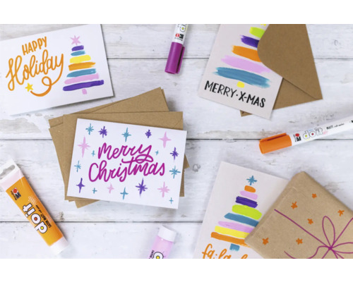 Szene mit selbstgemachten Weihnachtskarten, Stiften und Geschenkverpackung auf einem Holztisch.