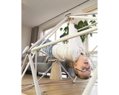 Junge hängt kopfüber an einem Indoor Klettergerüst im Wohnzimmer.