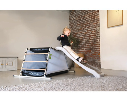 Kleinkind rutscht auf Spielplatzrutsche mit Klettergerüst im Innenbereich