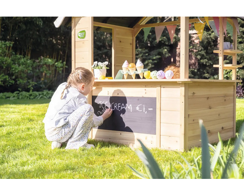 Fille écrit à la craie sur un magasin en bois dans le jardin.