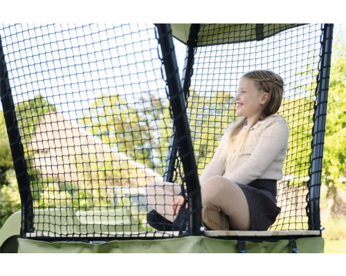 Mädchen sitzt lächelnd in einem sicheren Spielturm mit Netz